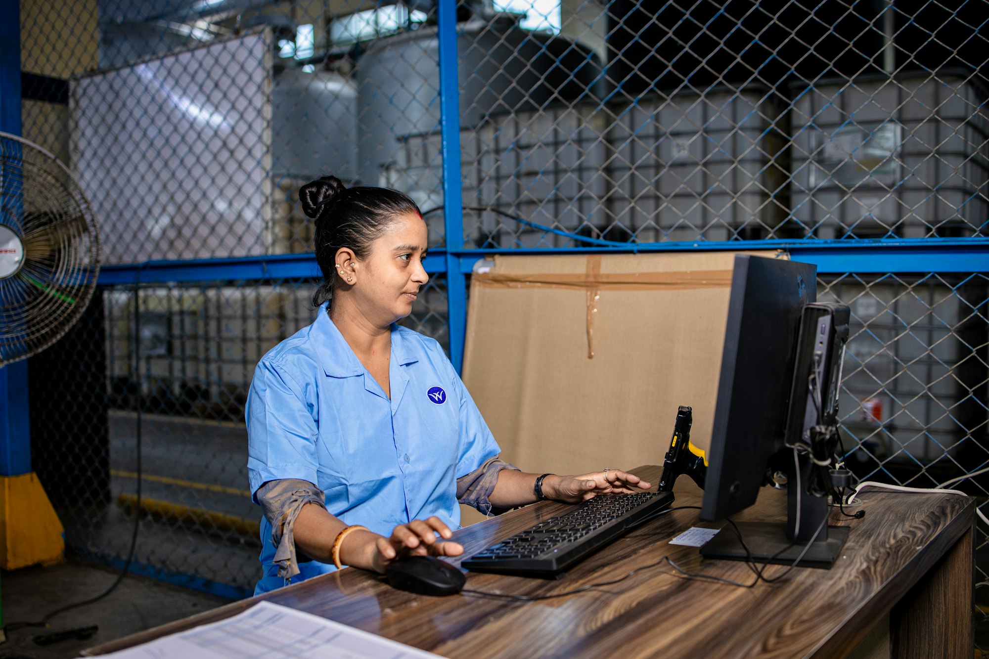 A logistics coordinator reviewing supplier orders at a computer in a warehouse